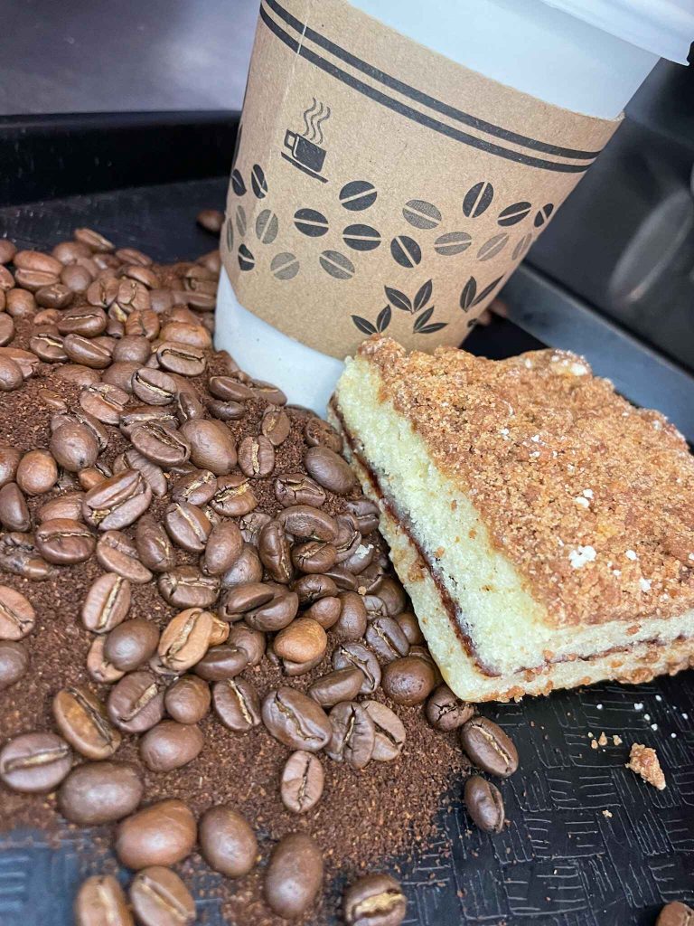 Cinnamon coffee cake surrounded by well-roasted coffee beans, coffee powder & coffee cup