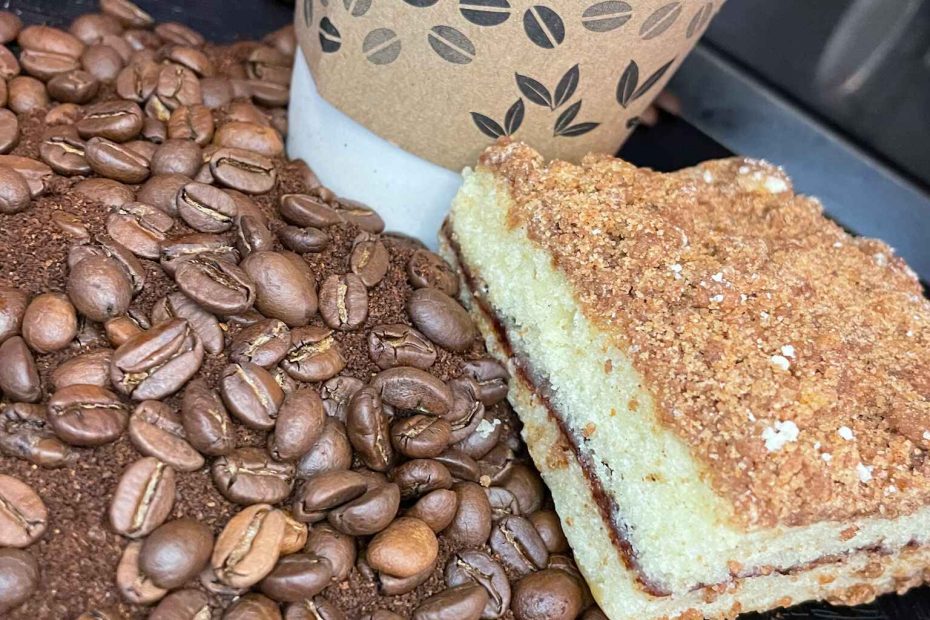 Cinnamon coffee cake surrounded by well-roasted coffee beans, coffee powder & coffee cup