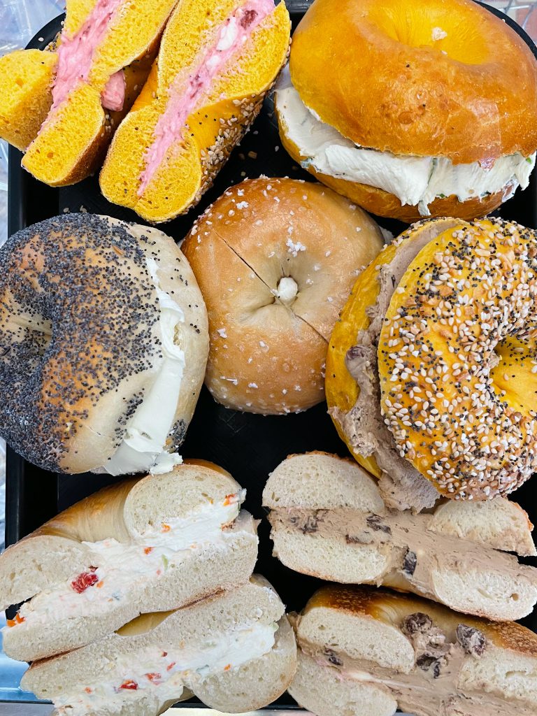Assorted bagels filled with different cream cheeses and spreads on a platter, including everything, poppy, and plain bagels.