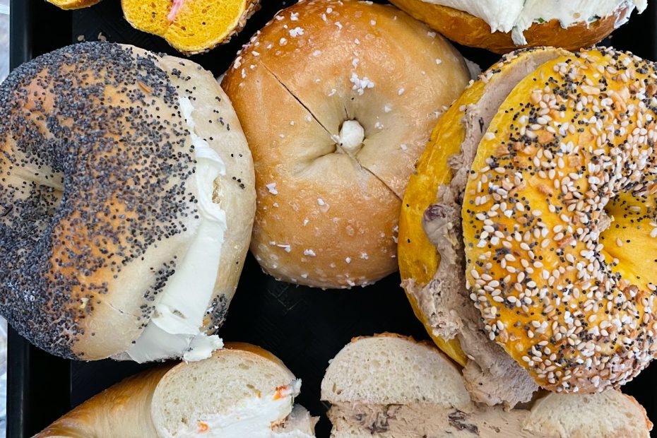 Assorted bagels filled with different cream cheeses and spreads on a platter, including everything, poppy, and plain bagels.