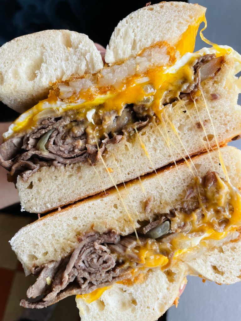 Steak, egg, and cheese bagel sandwich with crispy hash browns and melted cheddar.