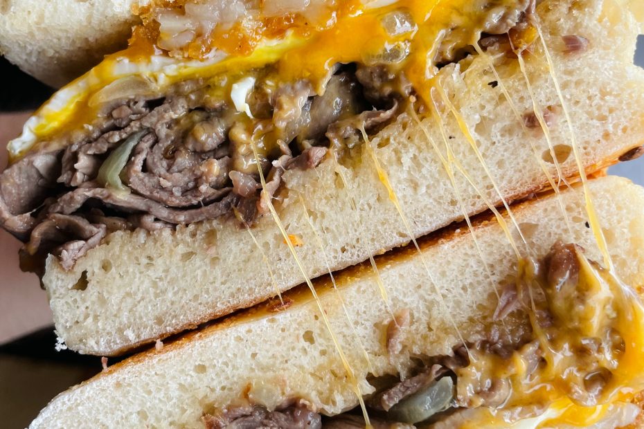 Steak, egg, and cheese bagel sandwich with crispy hash browns and melted cheddar.