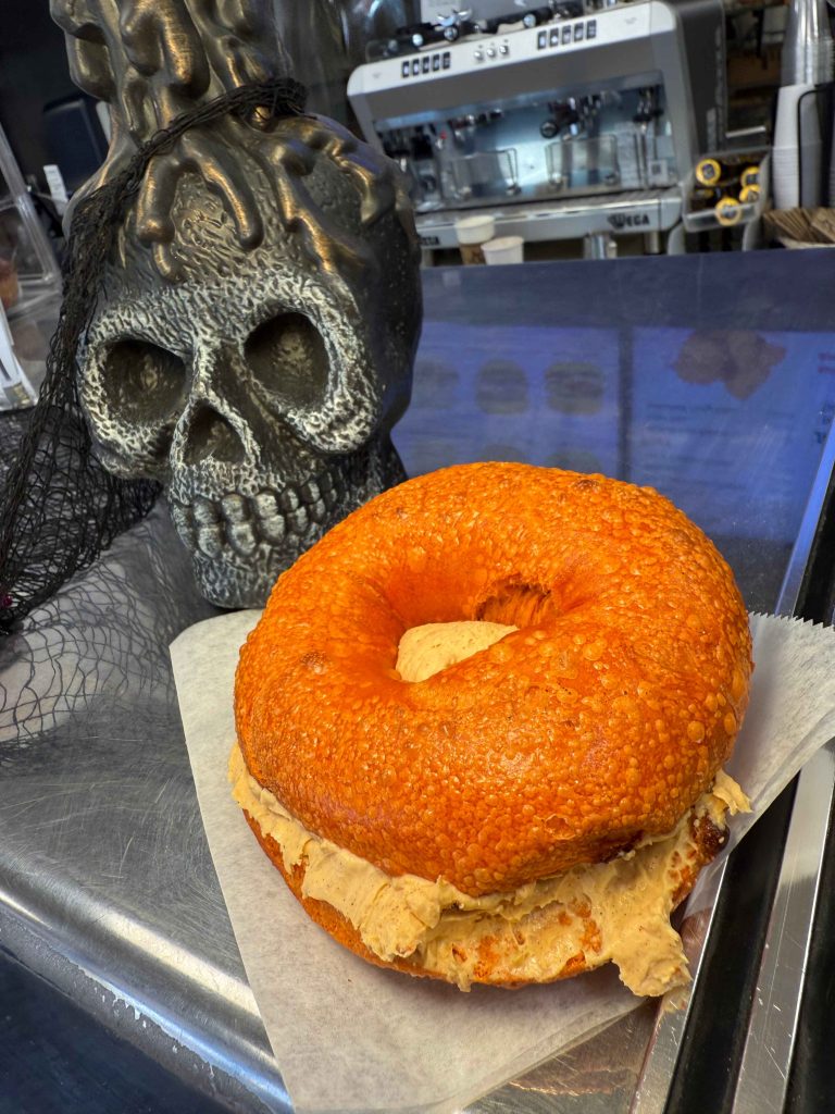 Halloween pumpkin bagel with creamy pumpkin spread beside a spooky skull decoration at Fast Bagel, New Jersey