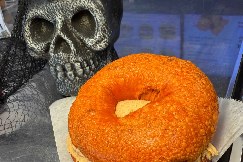 Halloween pumpkin bagel with creamy pumpkin spread beside a spooky skull decoration at Fast Bagel, New Jersey