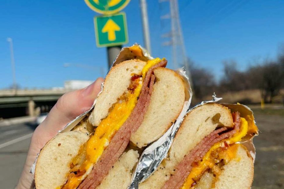 A fresh Pork Roll, egg, and cheese NJ breakfast sandwich held in front of a Garden State Parkway sign.