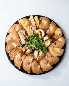 Sliced breakfast bagel sandwiches with egg and bacon arranged on a black platter for group catering.