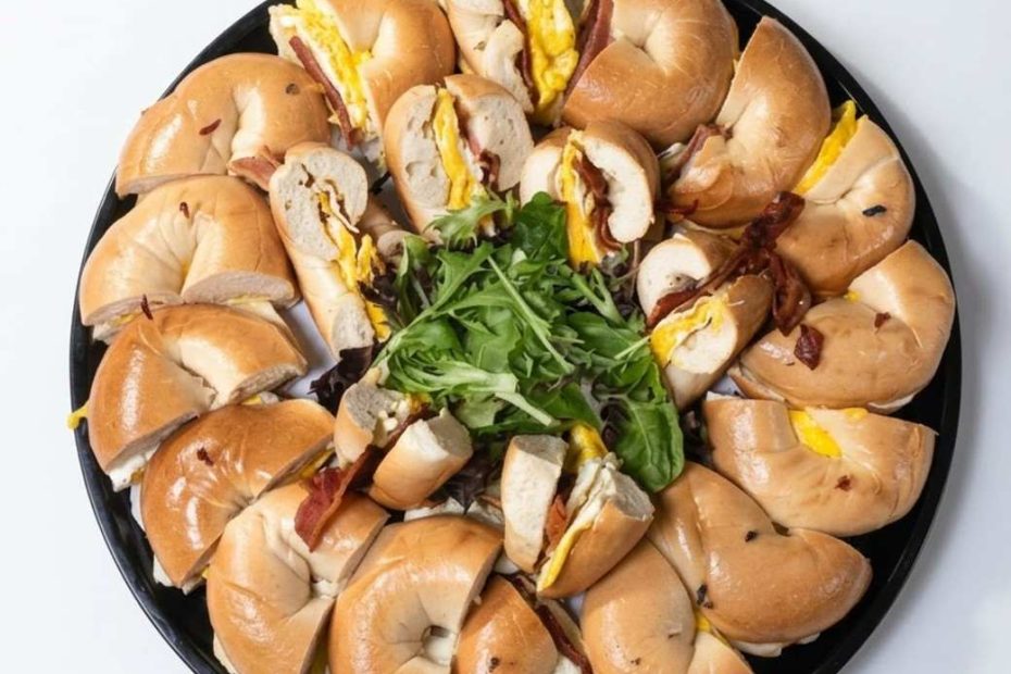 Sliced breakfast bagel sandwiches with egg and bacon arranged on a black platter for group catering.